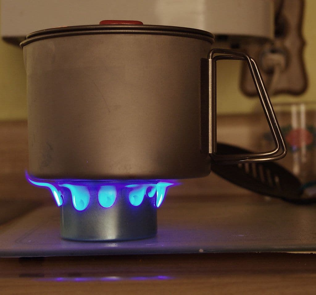 Titanium pot with a folding handle on a small stove, blue flames glowing beneath it