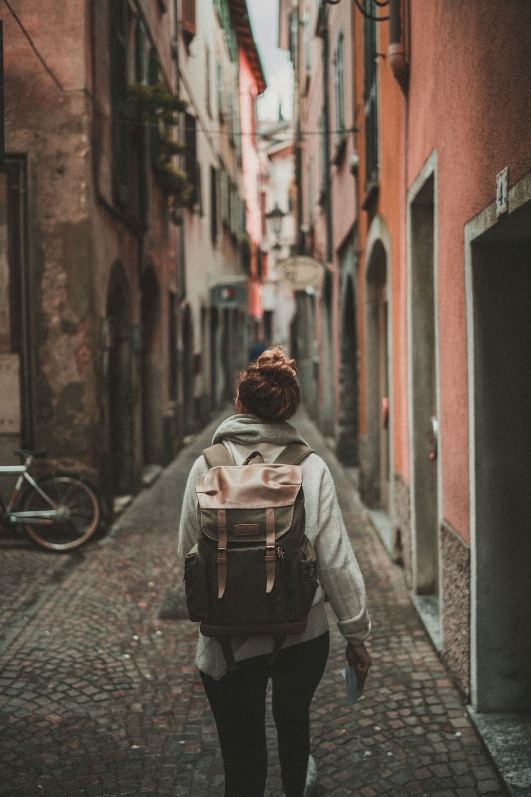 Metro 20L Daypack, alternate view: Woman wearing a sand-coloured daypack walking down a narrow old-town street