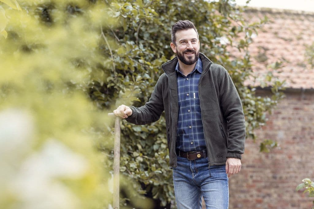 Hearth Fleece Jacket, alternate view: Smiling man in a charcoal fleece jacket over a plaid shirt in a garden