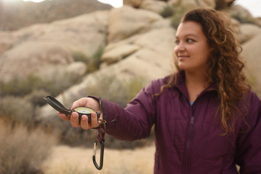 Thumbnail: Woman in a port-red fleece holding a compass among desert boulders