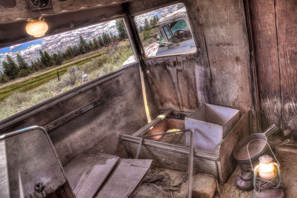 Thumbnail: Lantern casting warm light inside a weathered wooden cabin with a mountain view