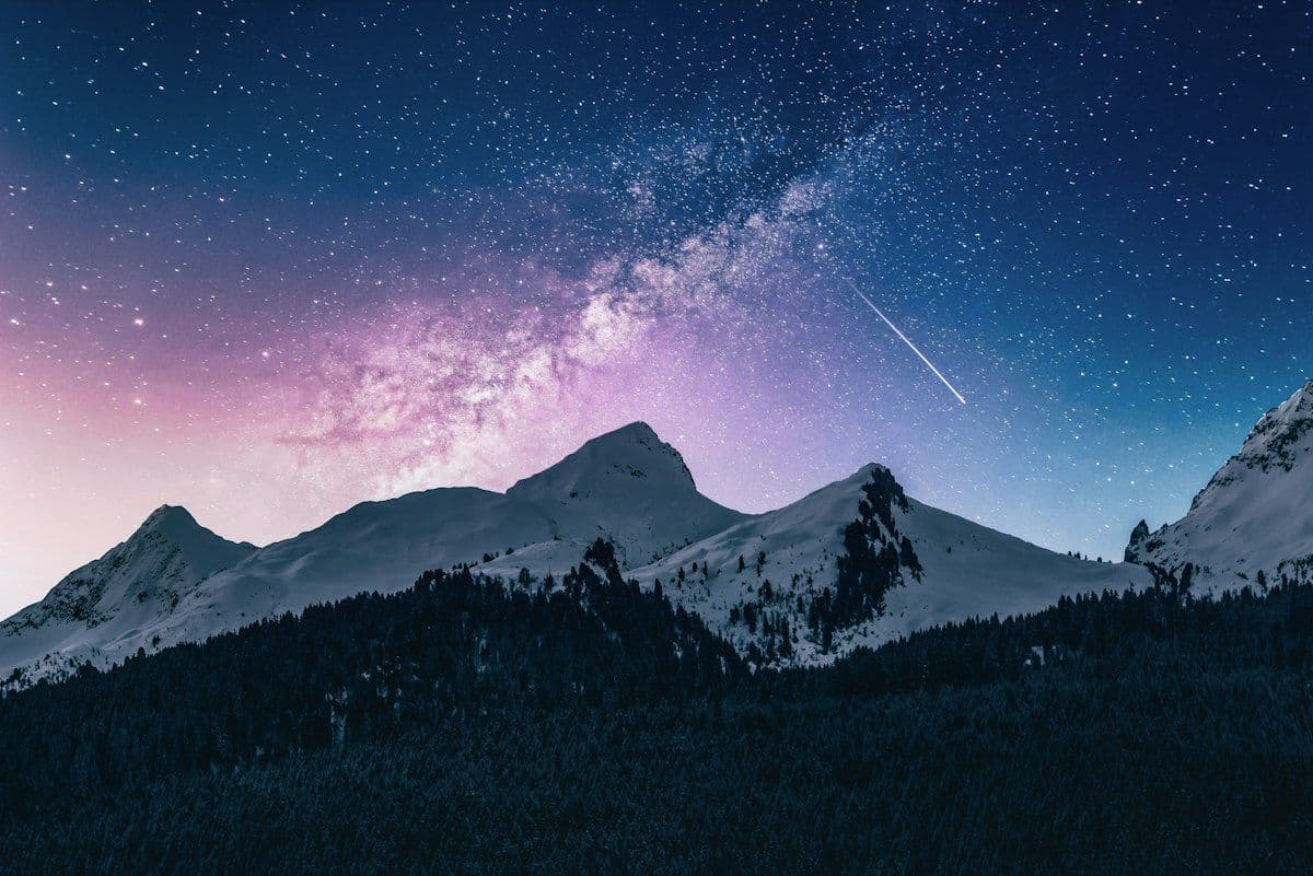Snow-capped mountain range under a starry night sky and the Milky Way