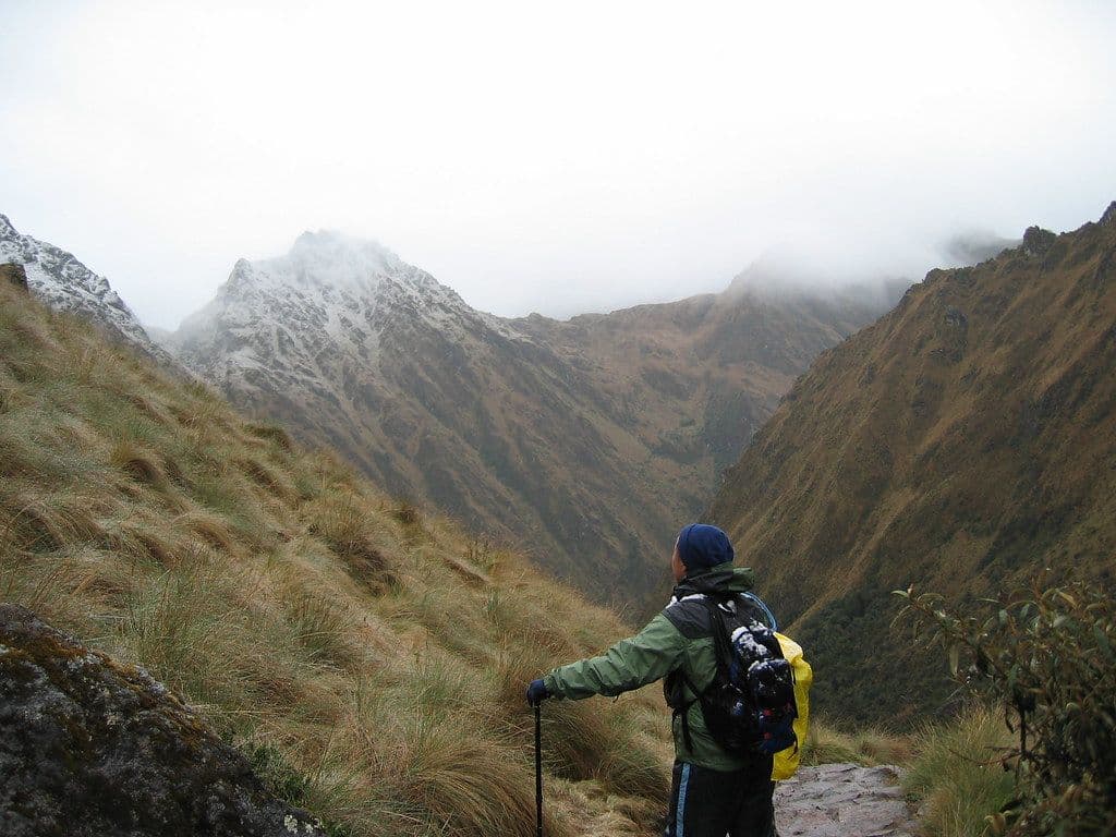 Trekker with a black and citron-yellow pack and trekking pole looking down a misty mountain valley