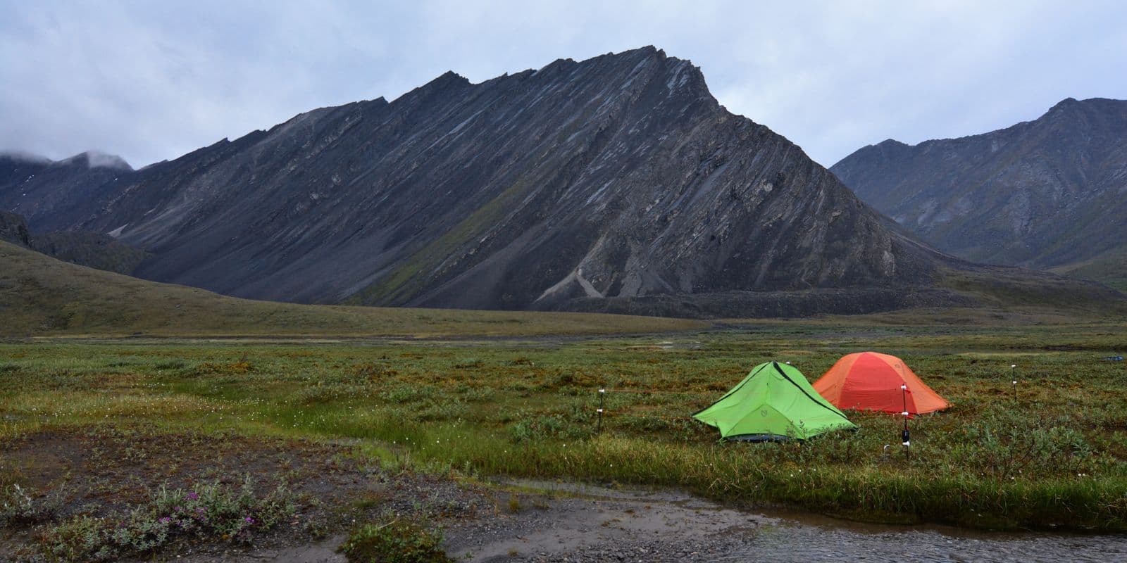 Skyline UL 1P Shelter, alternate view: Green and red tents pitched on tundra below dark mountain ridges