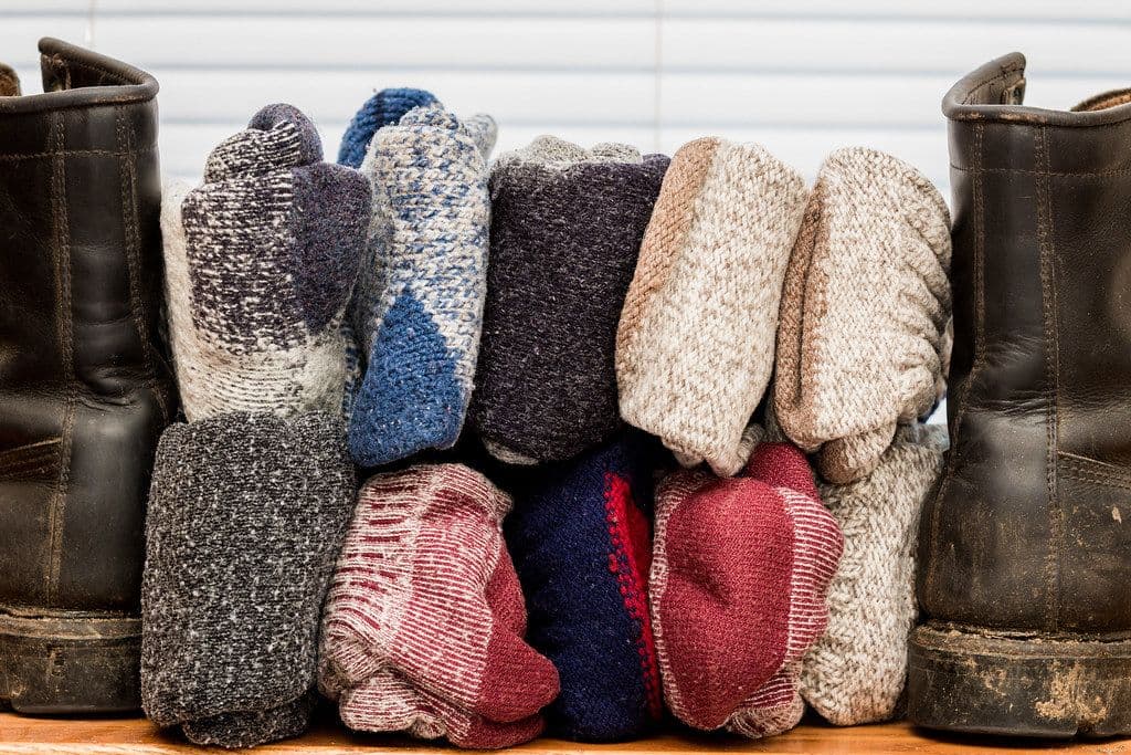 Stack of rolled wool hiking socks in heather, cranberry and navy between two leather boots