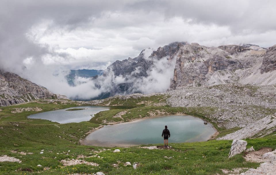 Lone hiker walking between turquoise alpine lakes beneath jagged Dolomite peaks