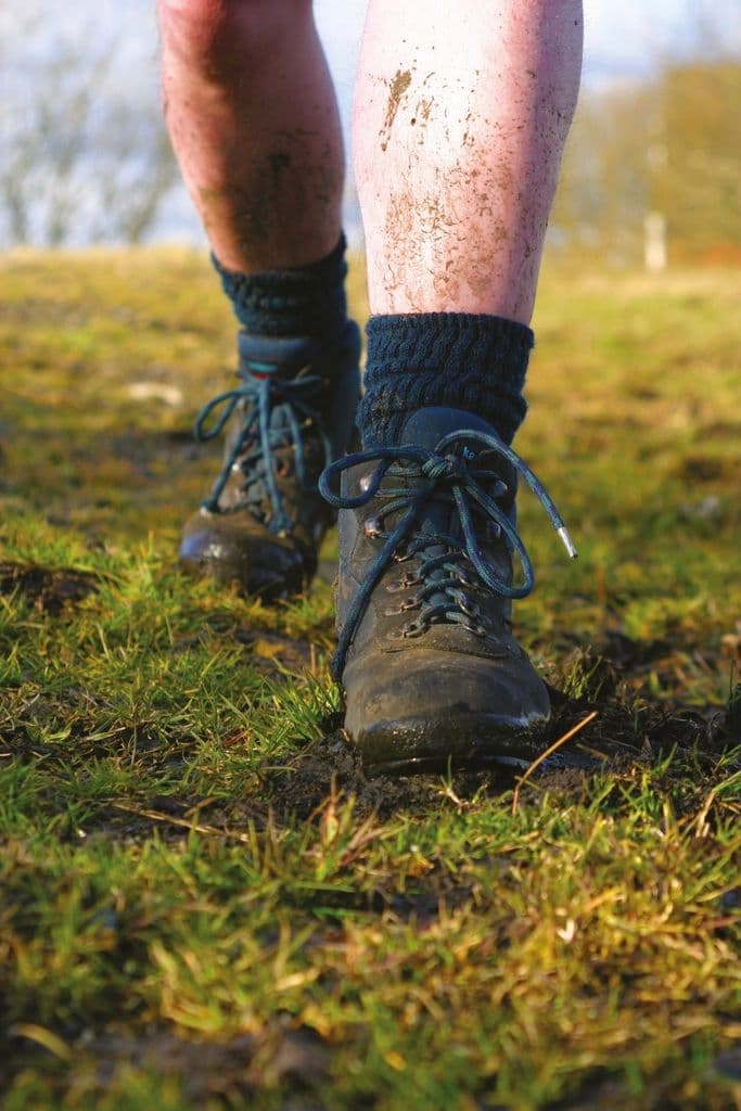 Thumbnail: Hiker striding across grass in slate-blue and brown mid boots with wool socks