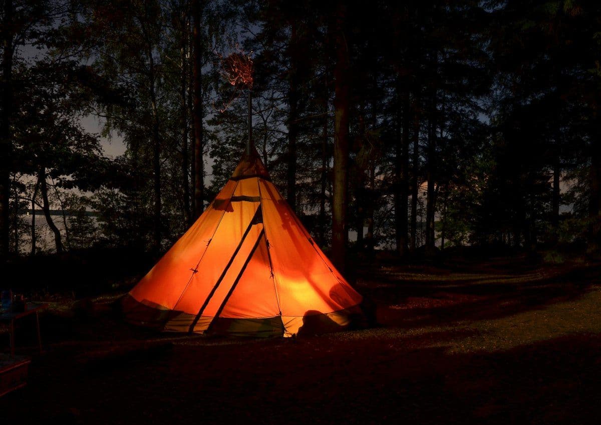 Orange tent glowing from inside in a dark forest