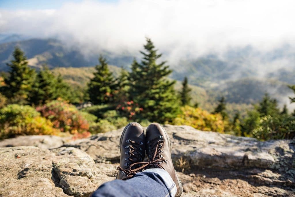 Hiking boots resting on a rock ledge above a forested, misty valley