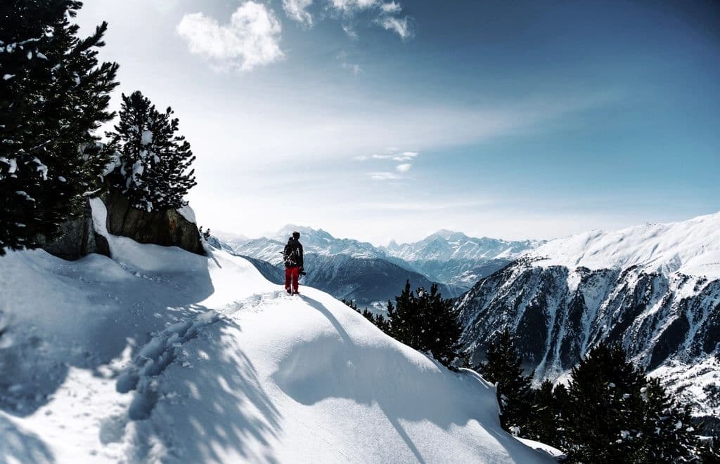 Hiker in a red jacket on a snowy ridge above a glacier valley